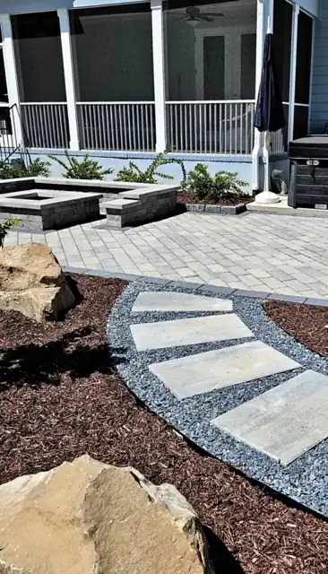 Curved paver patio and step below a screened porch, edged with grey gravel, boulders and fresh mulch