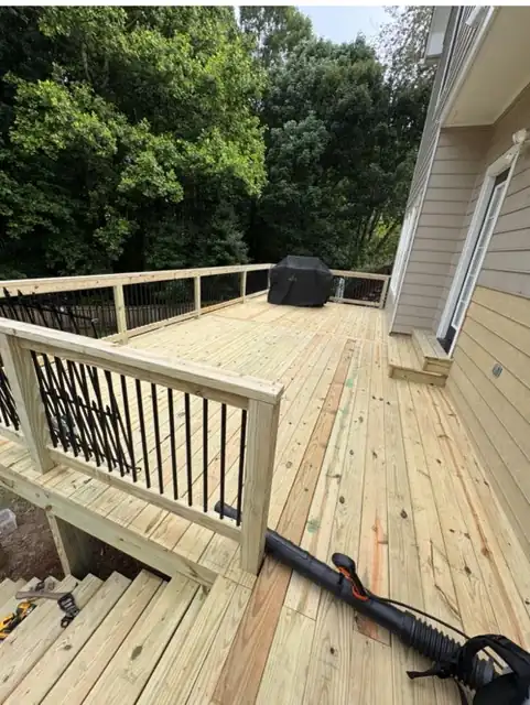 Newly built pressure-treated wood deck with railings and stairs at the back of a house