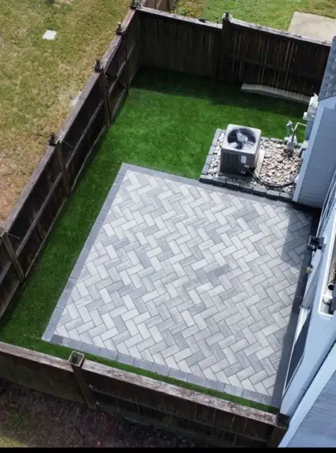Herringbone-pattern paver pad with a border course in a fenced backyard, seen from above