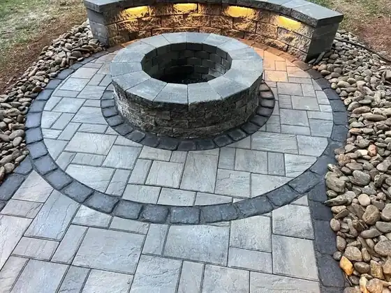 Circular paver patio with a stacked-stone fire pit in the centre, a dark border course and a seat wall with under-cap lighting