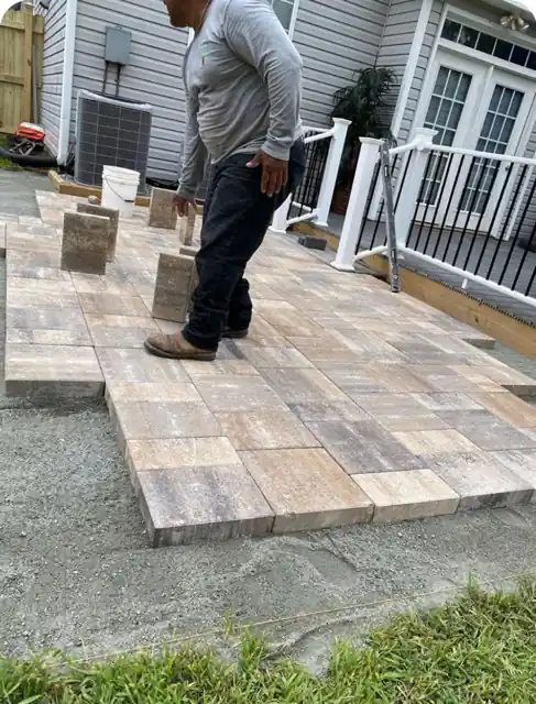 Crew member setting pavers on a screeded gravel base next to a new white deck railing