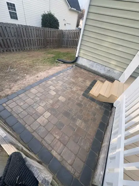 Multi-tone paver walkway with a dark border running along the side of a house