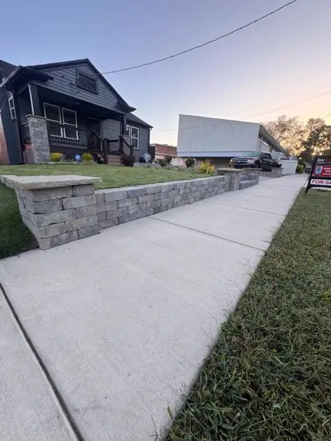 Concrete walkway running along a block retaining wall beside a dark-grey house