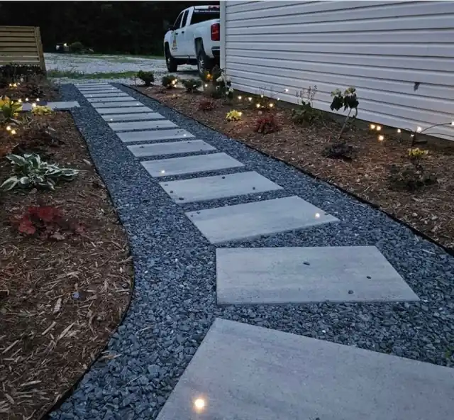 Concrete slab stepping-stone path set in grey gravel beside new shrubs, mulch beds and low path lights