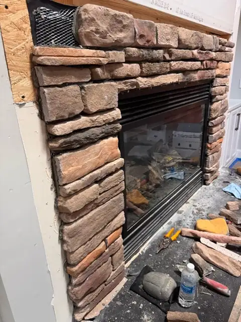 Stone veneer being fitted around a fireplace insert, with tools on the hearth